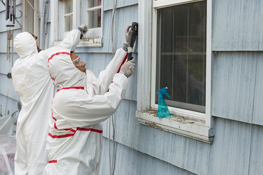 Abatement Contractor Insurance - Workers in Protective Gear While Removing Hazardous Materials From the Outside of Home