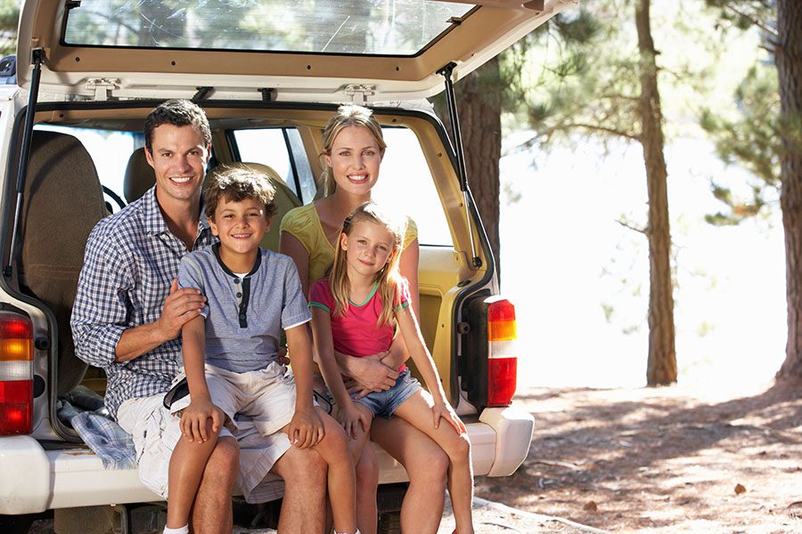 Personal Insurance - Closeup Portrait of a Cheerful Family with Two Kids Sitting in the Back Trunk of Their Car While on a Summer Vacation to the Lake